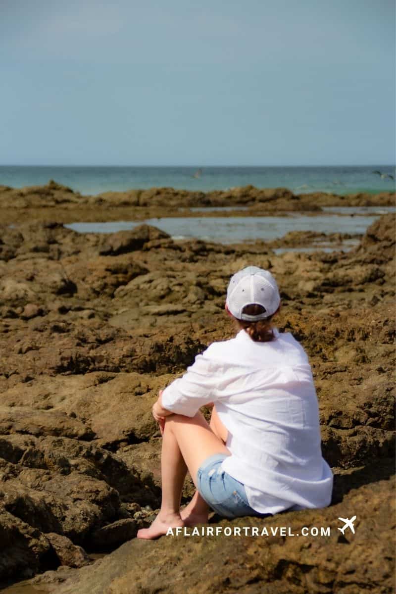 Woman in a white shirt and cap sitting on volcanic rock tide pools overlooking the ocean in Guanacaste