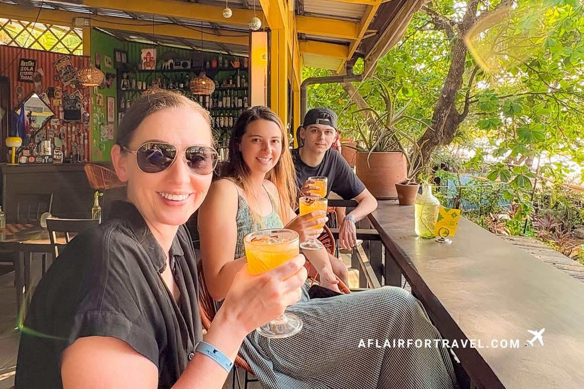 Three people smiling with orange cocktails at a colorful open-air bar in Costa Rica