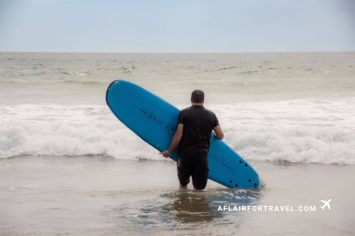 Man carrying a blue foam surfboard into the waves on a beach in Guanacaste